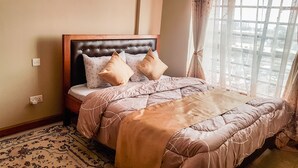 Een net opgemaakt bed met een hoofdeinde, een kamerkleed met patroon en een raam met gordijnen.