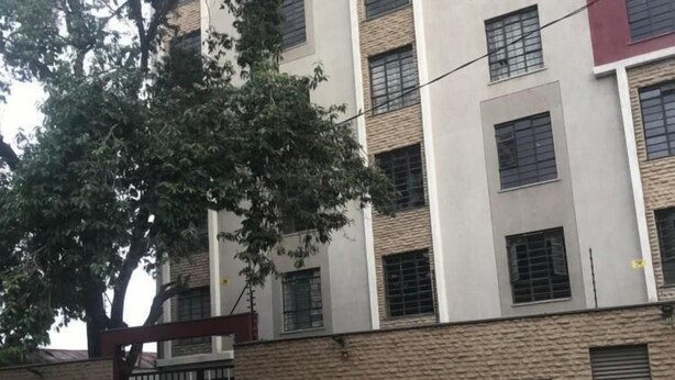 Een meerlaags gebouw met een hek en een bord met daarop 'West Suites', en een boom ervoor.