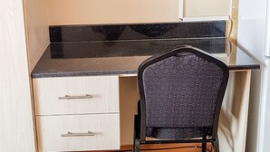 Een kleine kitchenette met een zwart aanrecht, een witte koelkast, een stoel en een aan de muur bevestigde televisie.