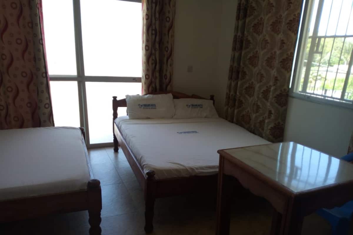 A room with two beds, a wooden table, and a window with patterned curtains.