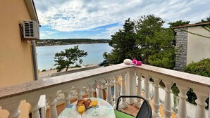En balkon med et bord dækket til morgenmad, med udsigt over vand og en fjerntliggende kystlinje.