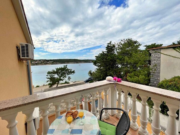 A balcony with a table set for breakfast, overlooking a body of water and a distant shoreline.
