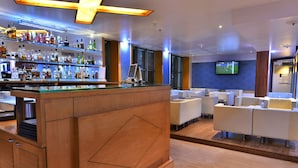 A modern bar area with a wooden counter and shelves of liquor bottles. There are white sofas and a TV mounted on the wall. - The Senator Hotel (Kolkata)