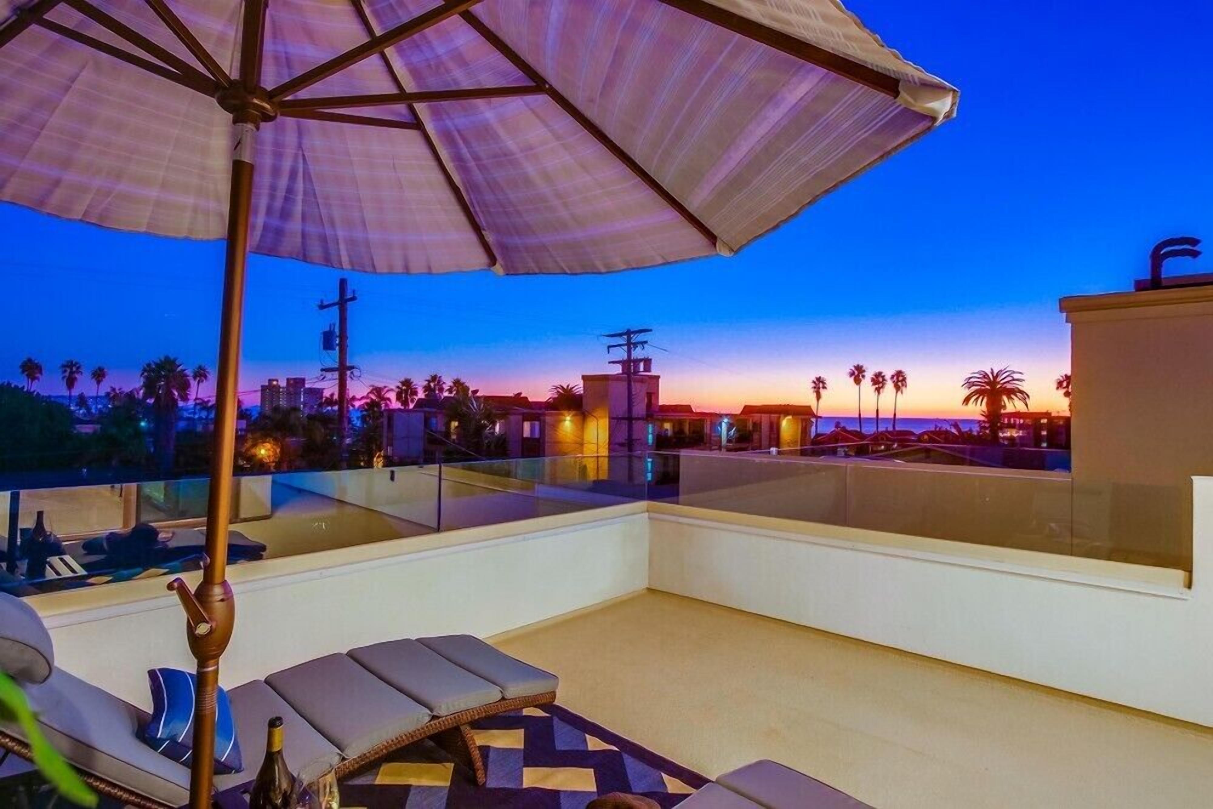 A rooftop terrace with lounge chairs, a table, and a large umbrella.