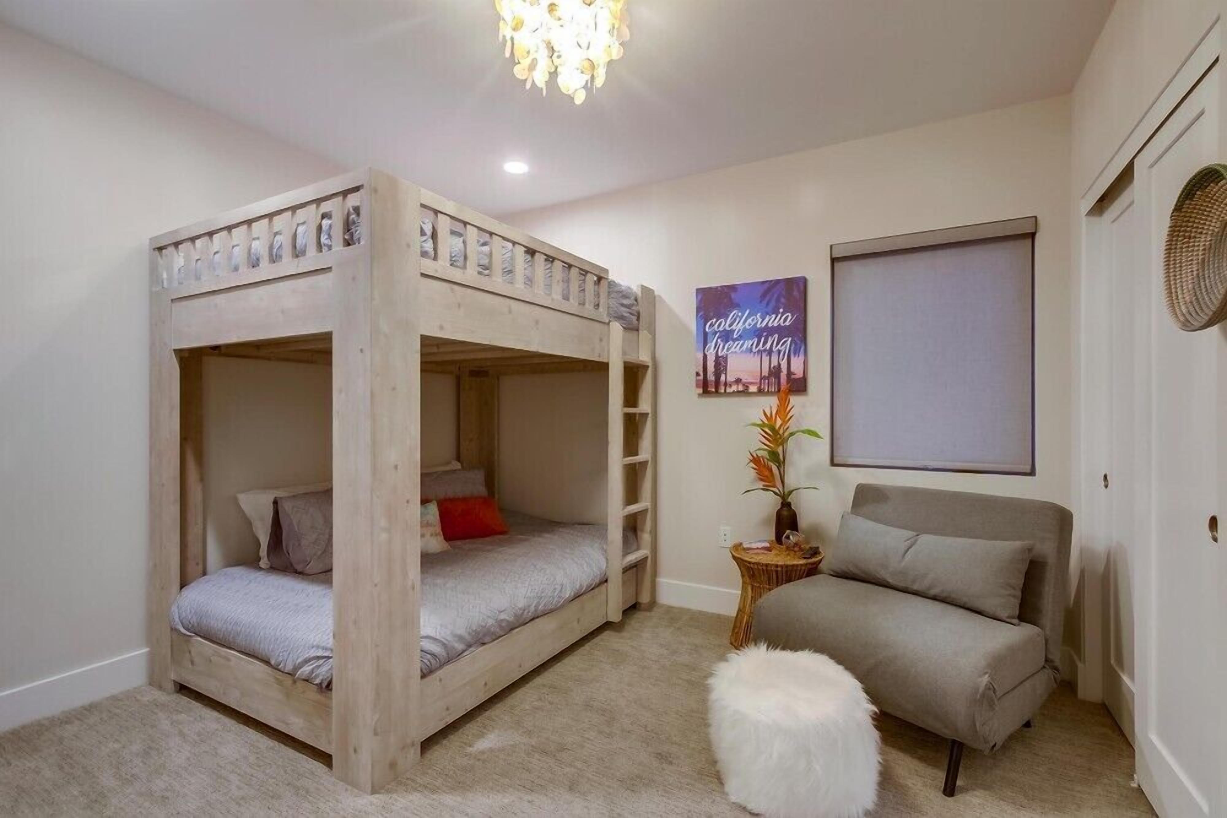 A room with a bunk bed, a sofa, a small side table with a plant, and a poster on the wall.