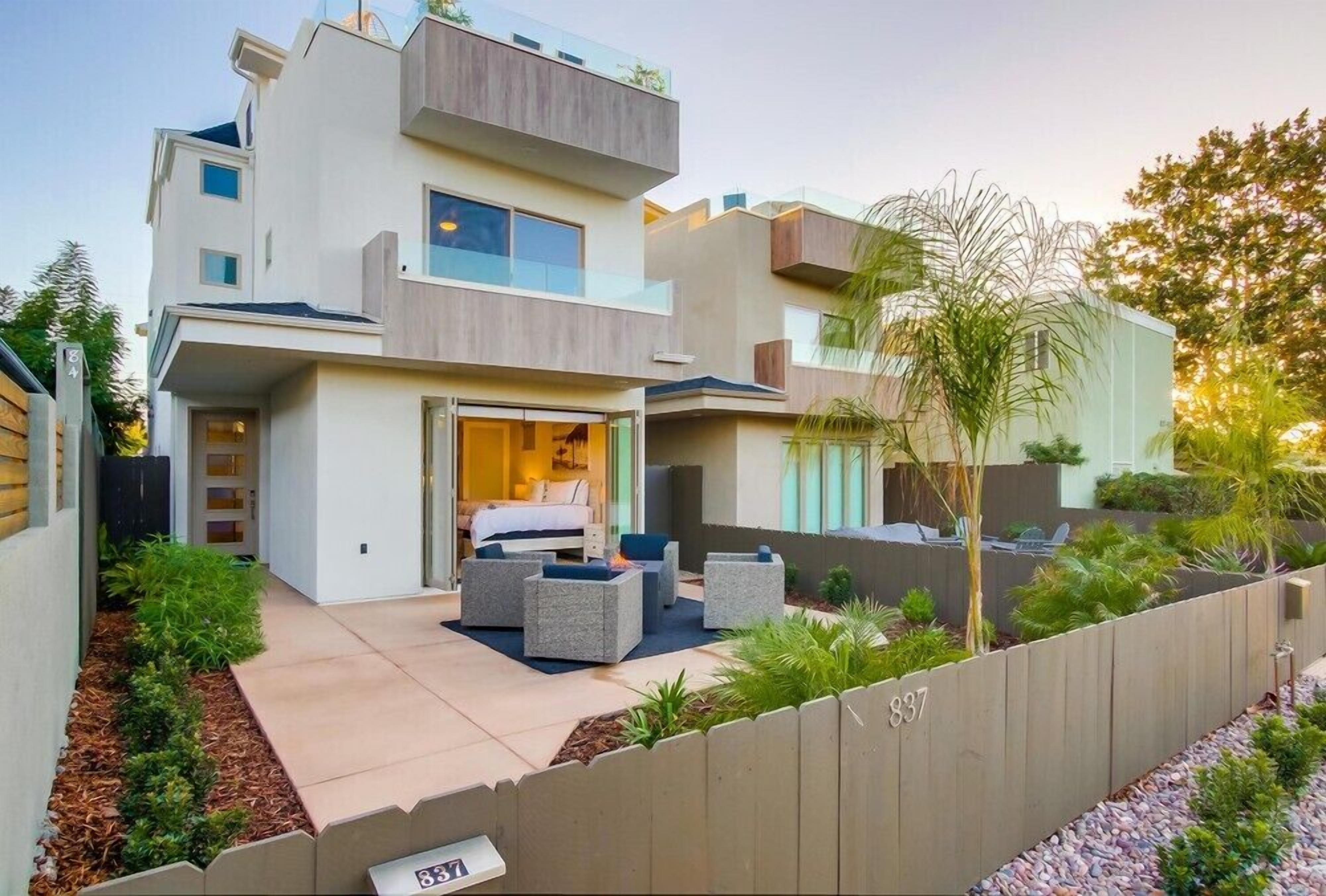 Une maison moderne à deux étages, dotée d’un balcon, d’un petit patio avec coin salon extérieur et d’un jardin bien entretenu.
