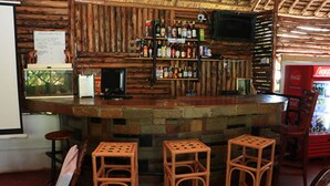 Una zona de bar rústica con paredes de madera, una barra de piedra y tres taburetes de mimbre.