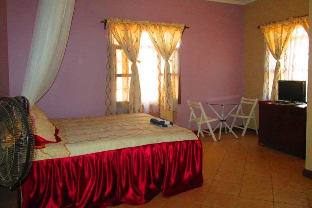 Un dormitorio con cama, escritorio, silla, ventilador y cortinas.