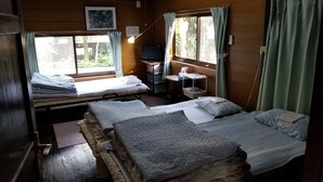 A cabin with two beds, a desk with a computer, and a window with curtains. - Hachijojima Gardenso (Hachijo)