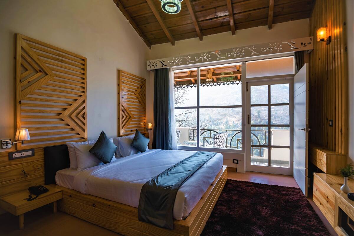 A bedroom with a large bed, wooden headboard, bedside tables, a nightstand, a window with a view, and a ceiling light fixture.