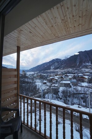 Un balcó de fusta amb vista a una vila i muntanyes cobertes de neu.