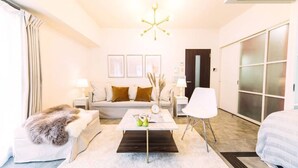 Moderni hotellihuone, jossa on sohva, sohvapöytä, valkoinen nojatuoli ja sänky.