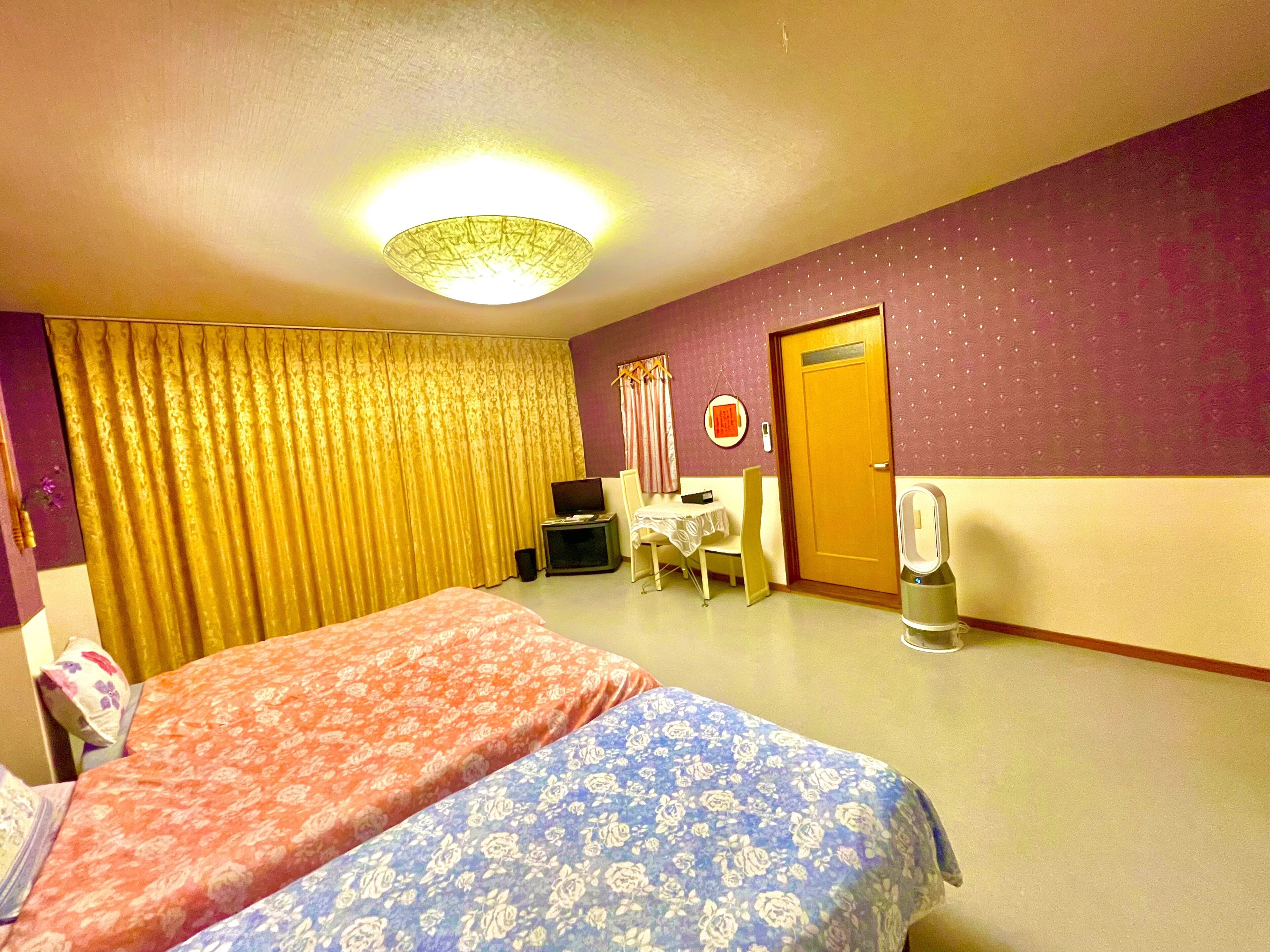 A hotel room with two beds, a desk, a chair, a television, and a door.
