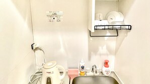 A compact kitchenette with a stove, sink, and a small shelf above the sink holding dishes. - Inuyama Modern Room (Inuyama)