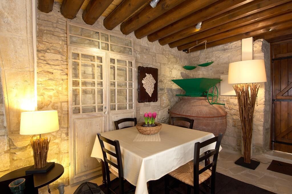 Zona pranzo con parete in pietra, travi in legno al soffitto, tavolo con sedie, una finestra e una grande pentola appesa al muro.