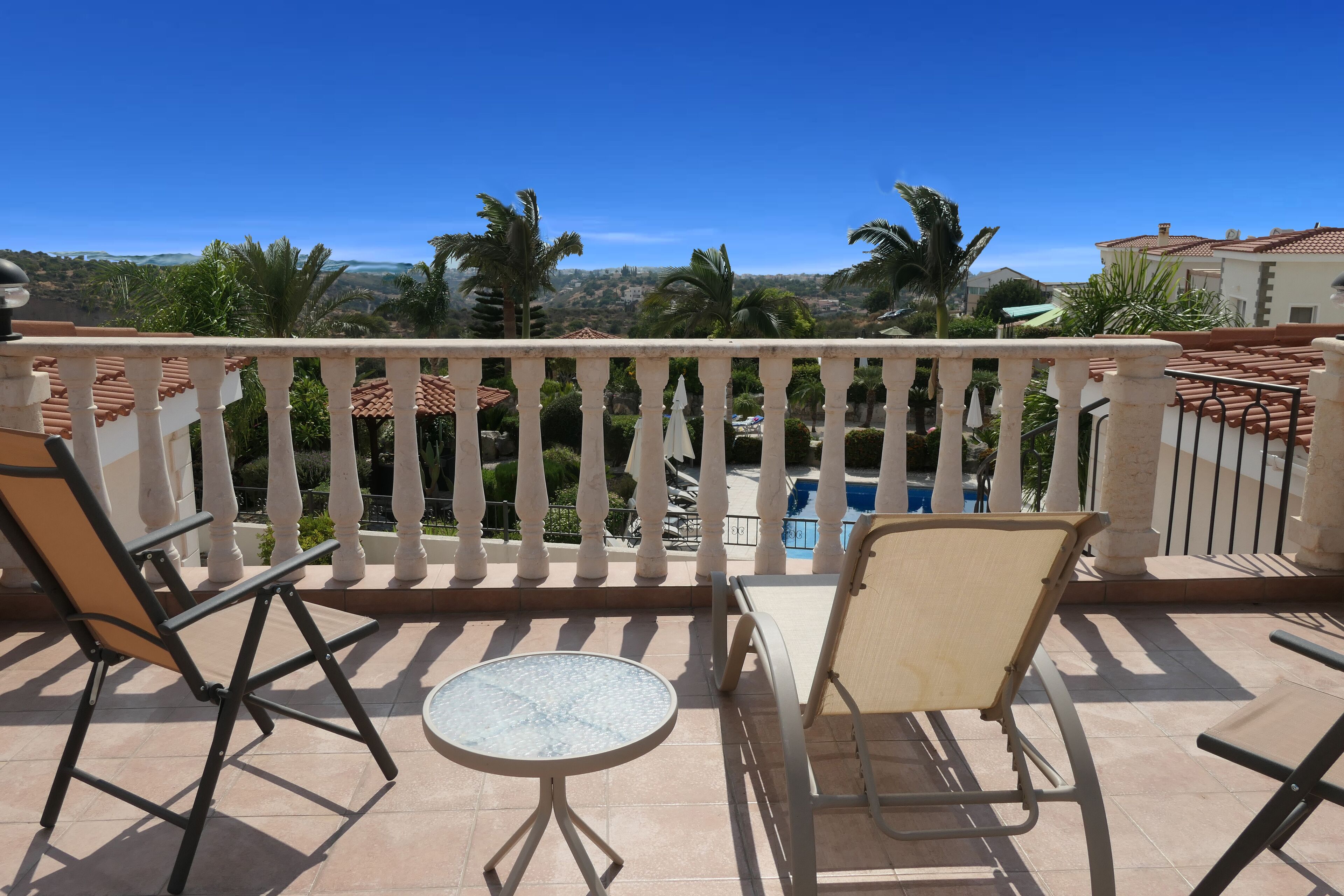 Un balcon avec deux chaises et une petite table, donnant sur une piscine et des palmiers.