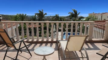Un balcon avec deux chaises et une petite table, donnant sur une piscine et des palmiers.