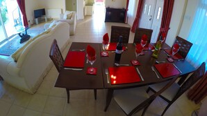 Uma sala de jantar com mesa posta para quatro pessoas, um sofá e uma TV ao fundo.