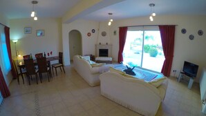 Uma sala de estar ampla com lareira, uma mesa de jantar com cadeiras e um conjunto de sofás.