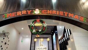 Entrada de un hotel con un cartel de 'MERRY CHRISTMAS', un adorno navideño y el nombre del hotel 'LALALAND'.
