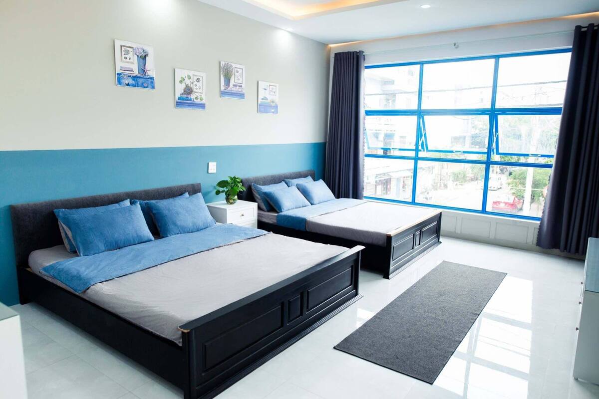 A modern hotel room with a large bed, a smaller bed, a desk, and a large window with curtains.