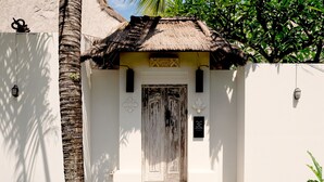A white building with a thatched roof entrance, a palm tree, and a sign with the number 3E. - Villa de Malicott (Seminyak)