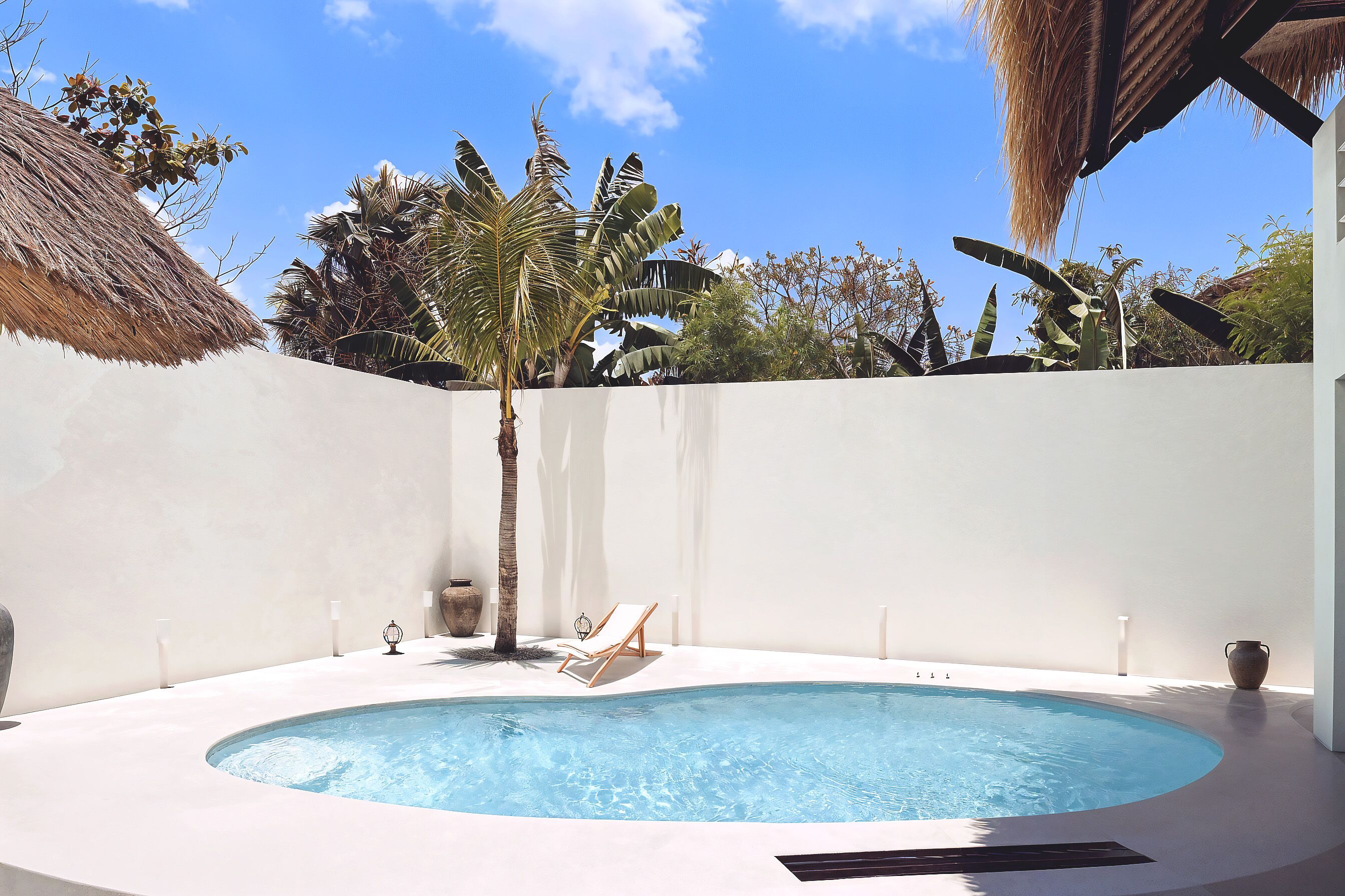 Une piscine circulaire avec un fauteuil de relaxation, entourée de murs blancs et de plantes tropicales.