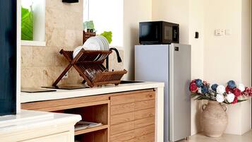 Una cocina con microondas, refrigerador, mueble de madera y un florero con flores.