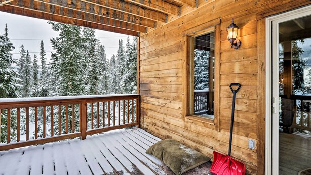 Eine Holzhütte mit einem Balkon, einem mit Schnee bedeckten Deck, einer roten Schaufel und einer Laterne.