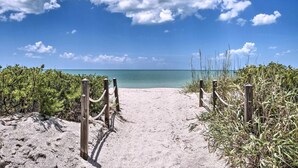 A sandy beach path leading to the ocean, surrounded by greenery and wooden posts.