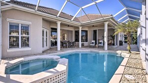 A covered outdoor pool area with a hot tub, patio furniture, and a view of the house.