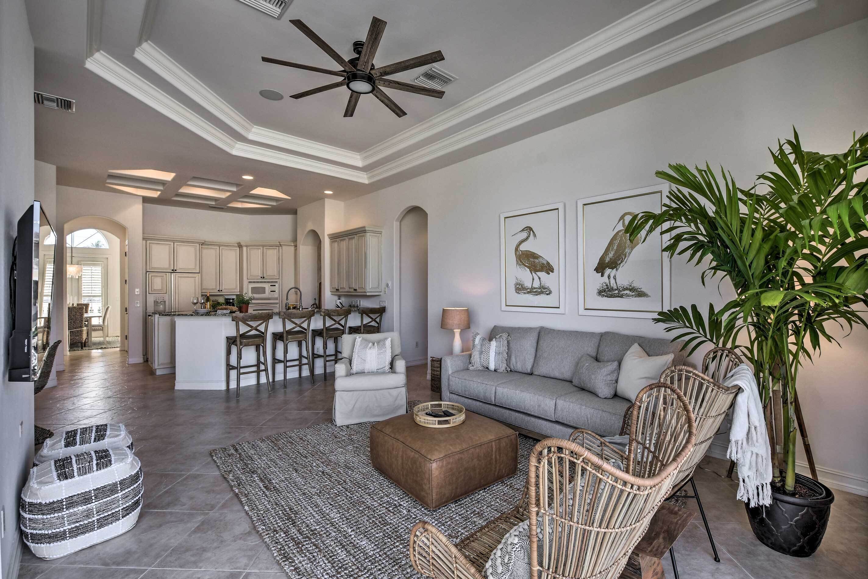 A spacious living room with a grey sofa, wicker chairs, a coffee table, and a large potted plant.