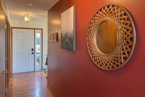 Un couloir avec un plancher en bois, une porte blanche, un tableau encadré et un miroir décoratif sur un mur rouge.