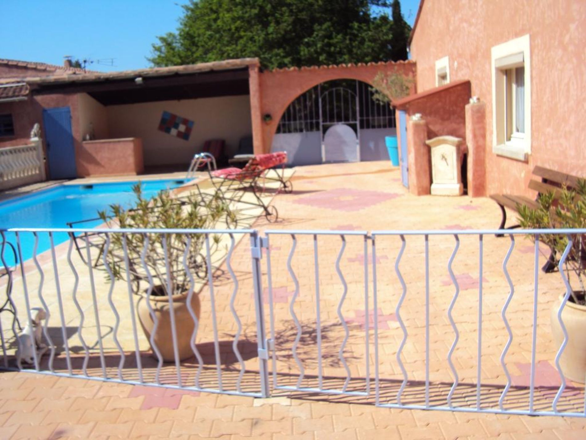 Una piscina con cerramiento metálico, plantas en macetas y un área de patio techada.