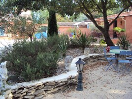 Un espace patio agrémenté de murs en pierre, d’une table et de chaises, le tout entouré de différentes plantes et arbres.