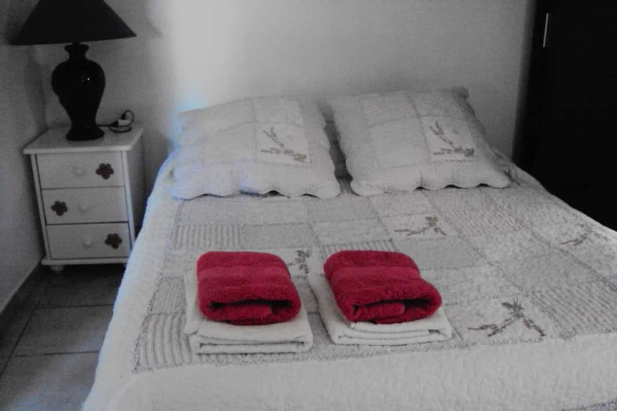 Cama bem arrumada com lençóis brancos e duas toalhas vermelhas colocadas ao pé da cama.