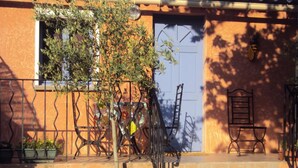 A building with a blue door, a small tree in a barrel planter, and two metal chairs on the porch. - Studio La Douloire (Pernes-les-Fontaines)