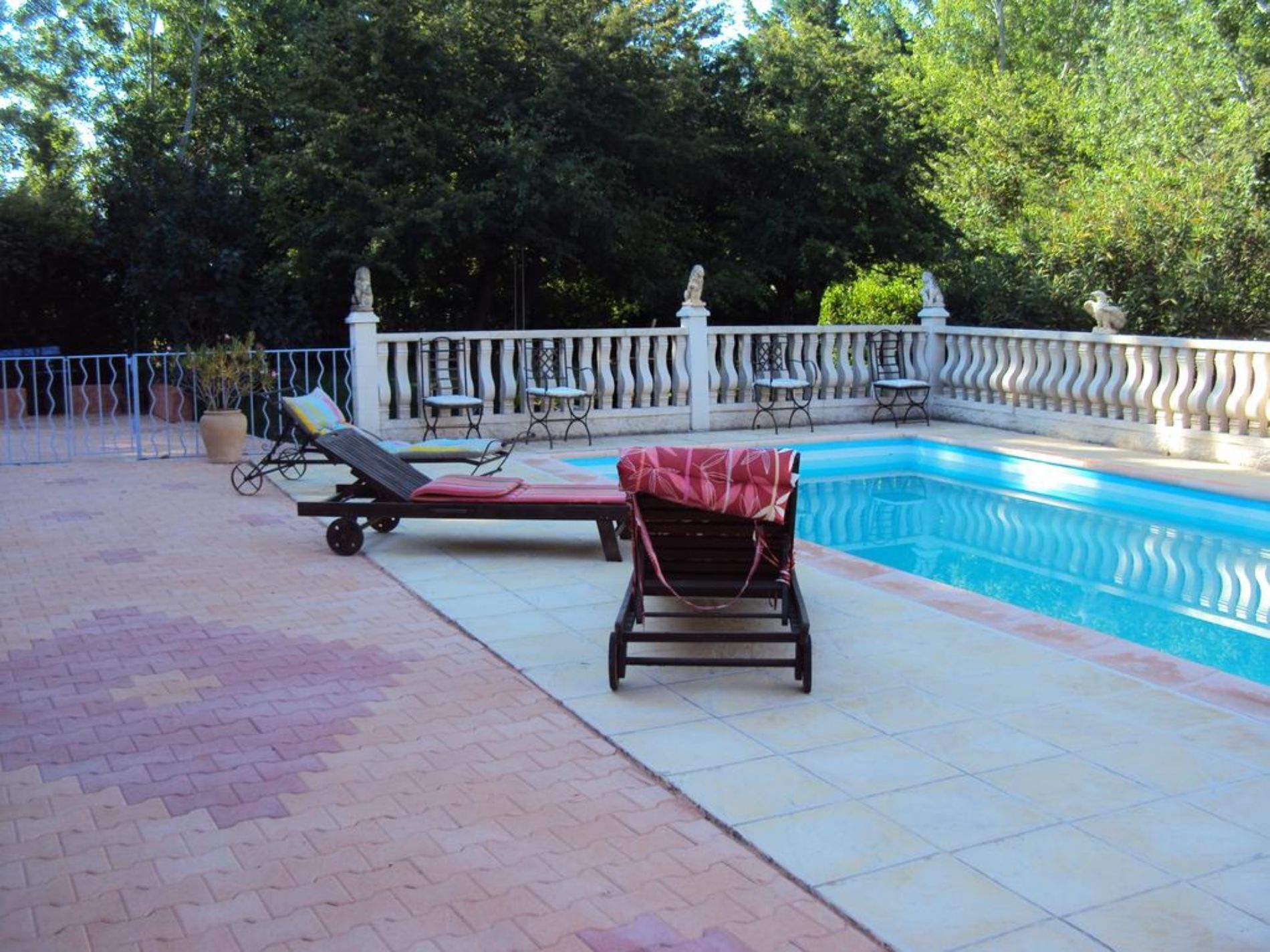 Ein Swimmingpool mit Liegestühlen und einem Sonnenschirm, umgeben von einem weißen Zaun und Bäumen.