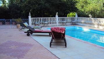 Ein Swimmingpool mit Liegestühlen und einem Sonnenschirm, umgeben von einem weißen Zaun und Bäumen.