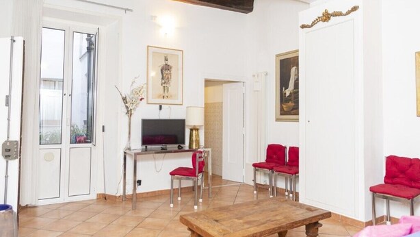 Una sala de estar con una mesa de centro de madera, sillas rojas, un televisor y obras de arte en las paredes.