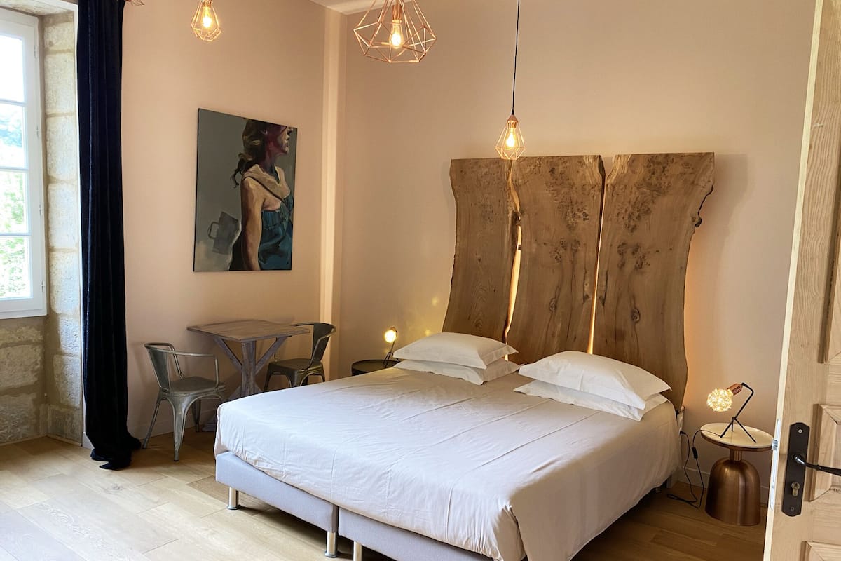 Un dormitorio con una cama grande, una mesita, una silla y un cuadro en la pared.