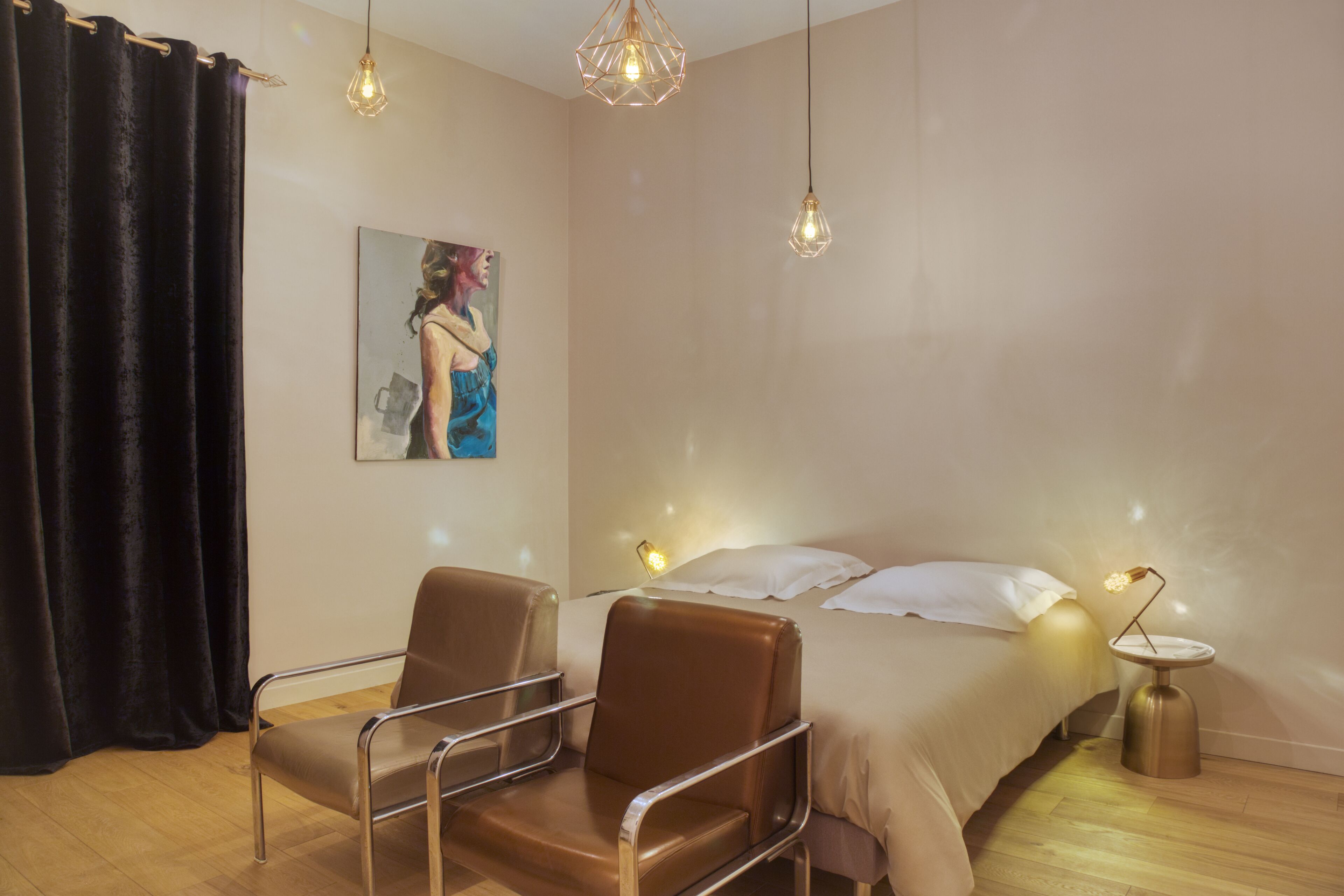 A hotel room with a bed, two armchairs, a painting on the wall, and a small table with a lamp.
