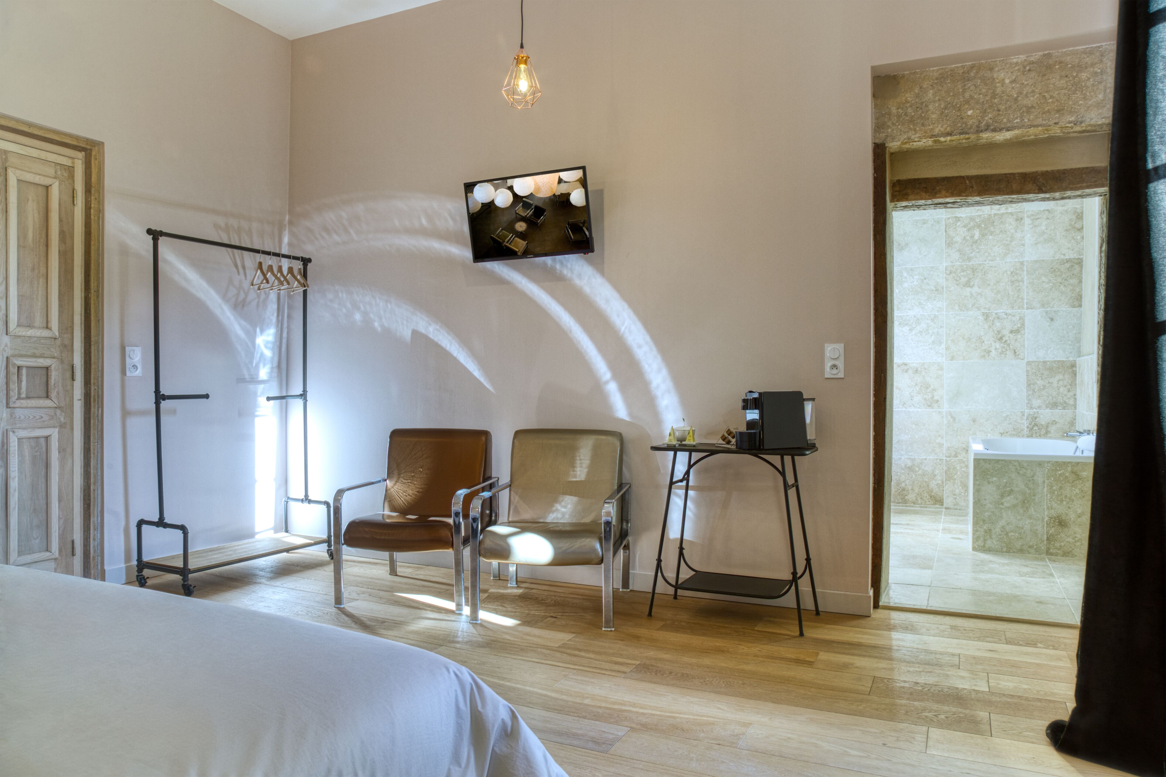 Une chambre d’hôtel comprenant un lit, deux chaises, une petite table, un téléviseur fixé au mur et donnant sur la salle de bain.