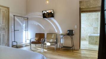 Une chambre d’hôtel comprenant un lit, deux chaises, une petite table, un téléviseur fixé au mur et donnant sur la salle de bain.