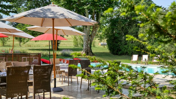 Une terrasse extérieure aménagée avec des meubles en osier, des parasols et une piscine.