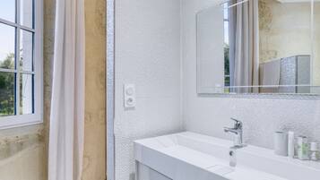 Een moderne badkamer met een wit wastafelmeubel, een grote spiegel en een raam met gordijnen.