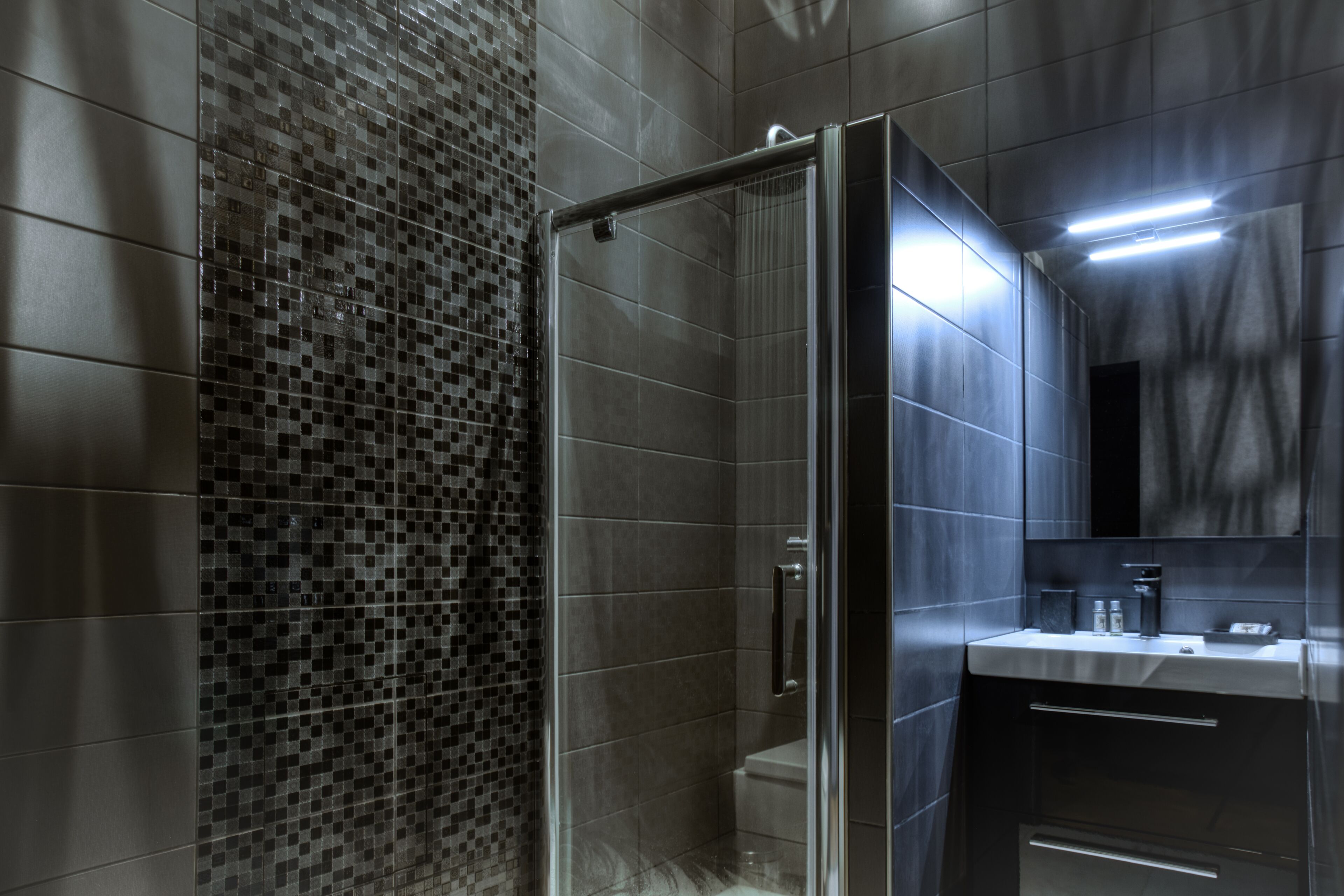 A modern bathroom with a glass-enclosed shower, tiled walls, and a vanity with a mirror.