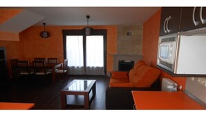 A living room with a sofa, coffee table, and dining area with chairs. There is a fireplace and a television mounted on the wall. - Stone Cottage III (Canencia)