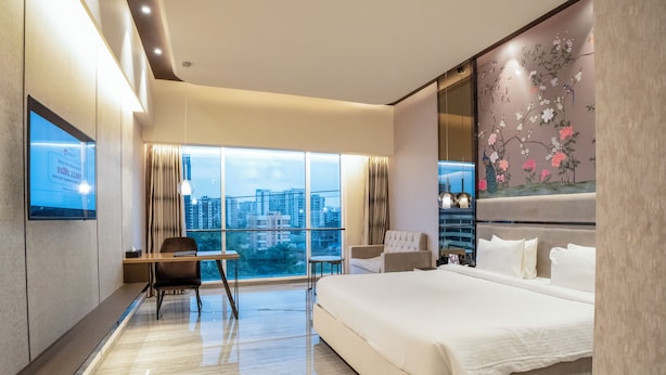 A modern hotel room with a large bed, a desk, and a view of the cityscape. - Seven Eleven Club (Mumbai)