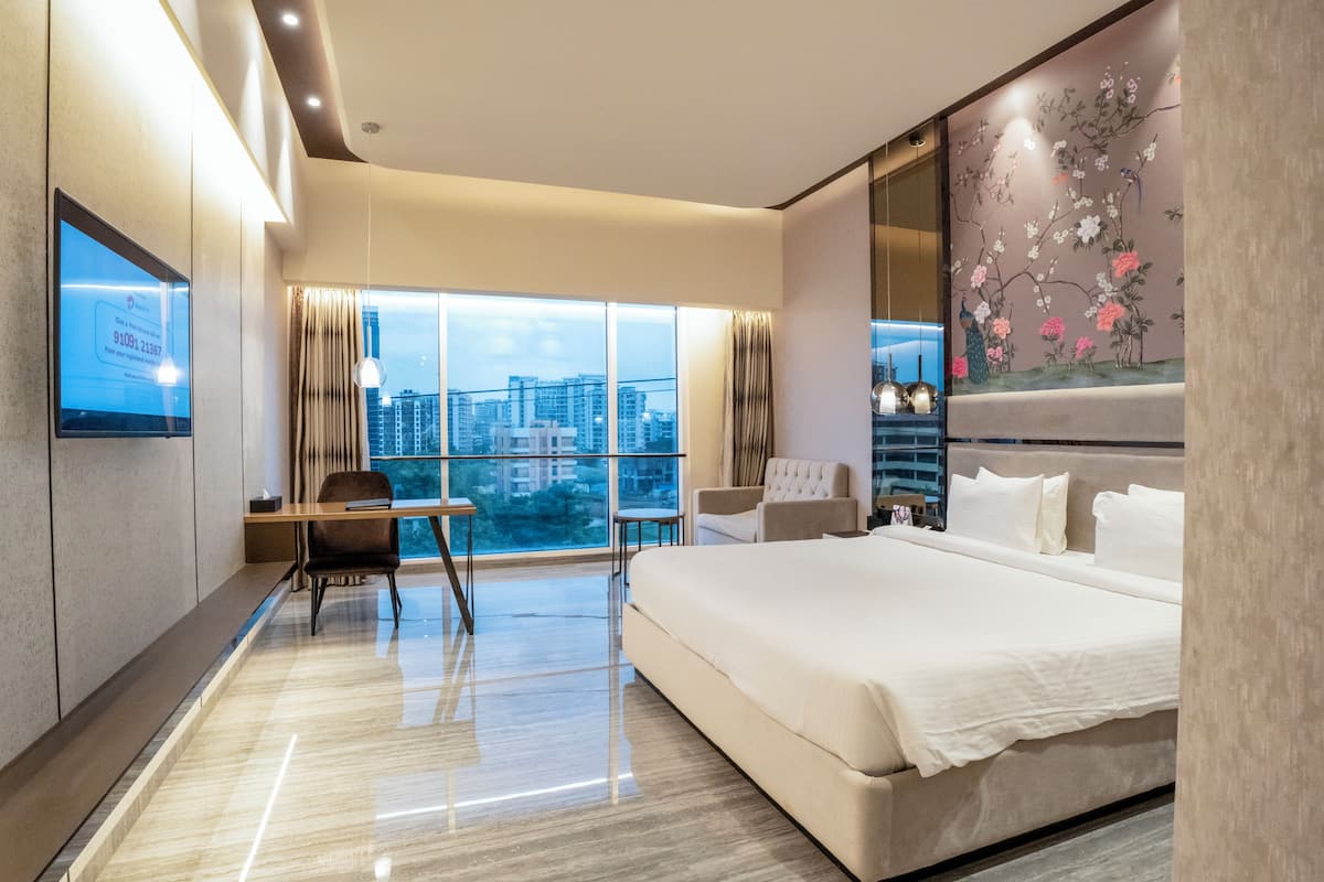 A modern hotel room with a large bed, a desk, and a view of the cityscape.